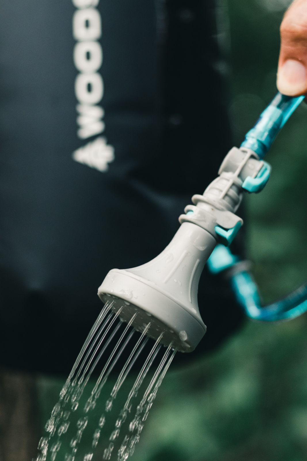 Portable camp shower head with blue hose spraying water outdoors